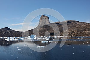 Many icebergs drift and melt in a fjord with a monolith in the background