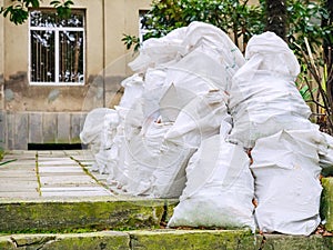 Many identical white bags with unnecessary old rubbish are piled up near the house