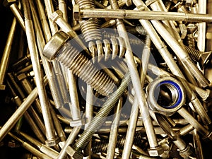 Many iron fasteners laying on top of each other with a big bolt at the front in a pile