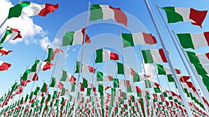 Many Italy flags on flagpoles against blue sky.