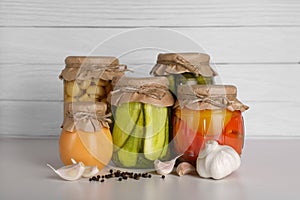 Many jars with different preserved vegetables and mushrooms on light grey table