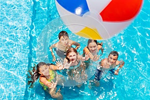 Group of children in pool lift hands, throw ball