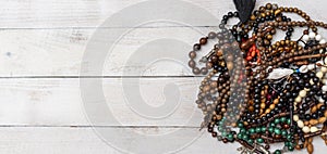 Many kind of Rosaries in different colors and sizes on white wooden background. Top view.