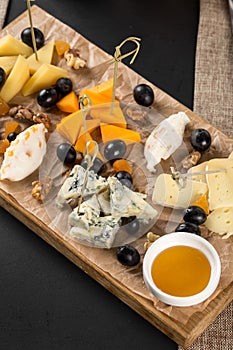 Many kinds of cheese with honey on wooden platter on the table at restaurant