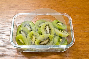 Many kiwi slices in a glass crisper on a wooden table. Kiwifruit slices without peel