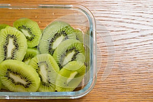 Many kiwi slices in a glass crisper on a wooden table. Kiwifruit slices without peel