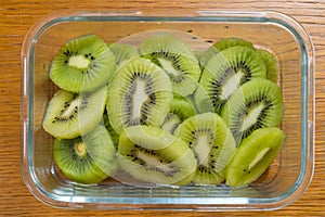 Many kiwi slices in a glass crisper on a wooden table. Kiwifruit slices without peel