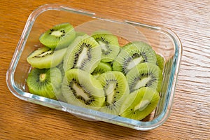 Many kiwi slices in a glass crisper on a wooden table. Kiwifruit slices without peel