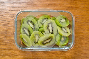 Many kiwi slices in a glass crisper on a wooden table. Kiwifruit slices without peel