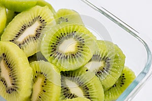 Many kiwi slices are placed in a glass crisper. Kiwifruit slices without peel