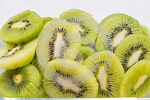 Many kiwi slices are placed in a glass crisper. Kiwifruit slices without peel