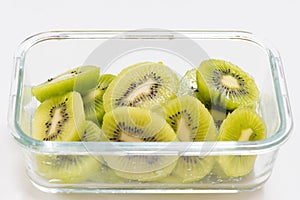 Many kiwi slices are placed in a glass crisper. Kiwifruit slices without peel