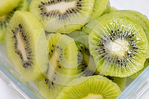 Many kiwi slices are placed in a glass crisper. Kiwifruit slices without peel