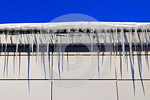 Many large and sharp icicles hang on the roof of the house