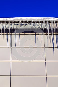 Many large and sharp icicles hang on the roof of the house