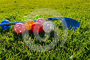 Many light colorful practicing plastic golf balls with holes and one golf club lays together at green grass. Practicing golf at