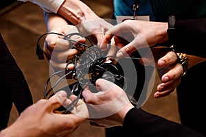 Many male hands try to untangle the wires