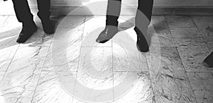 Many men`s leg wearing black slacks or long trousers and black leather shoes and standing on marble floor in black and white tone photo