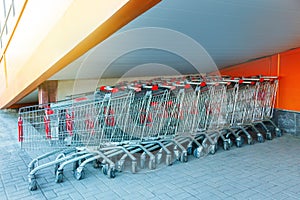 Many metal shopping carts on a parking lot near supermarket outdoors