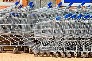 Many metal shopping carts on a parking lot near supermarket outdoors. Shopping concept