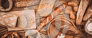 Many mixed baked breads and rolls on rustic wooden table