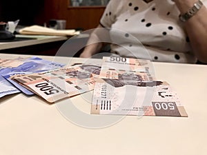 Many mixed Mexican peso bills spread over a beige desk