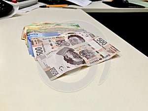 Many mixed Mexican peso bills spread over a beige desk