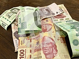 Many mixed Mexican peso bills spread over a wooden desk