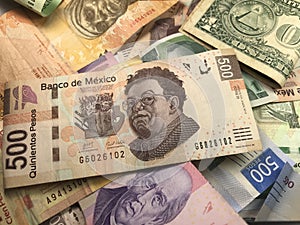 Many mixed Mexican peso bills spread over a wooden desk