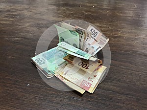 Many mixed mexican peso bills spread over a wooden desk