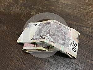 Many mixed mexican peso bills spread over a wooden desk