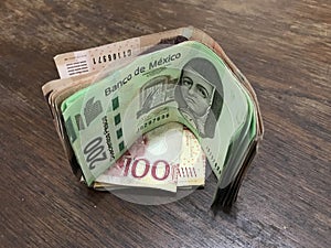 Many mixed mexican peso bills spread over a wooden desk