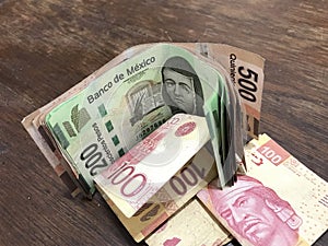 Many mixed mexican peso bills spread over a wooden desk