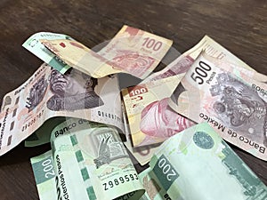 Many mixed mexican peso bills spread over a wooden desk