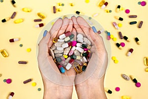 Many multi-color pills in the hands of a woman against the background.