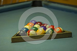 A Many multicolored blurred billiard balls with numbers lie on the table with a blue cloth in a wooden pyramid. billiard table