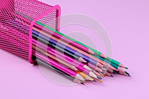Many multicolored pencils fall out of the glass on a pink background. School supplies