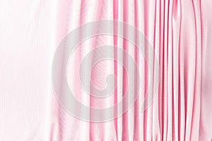 Many narrow vertical folds on a delicate pink fabric turn into a smooth background