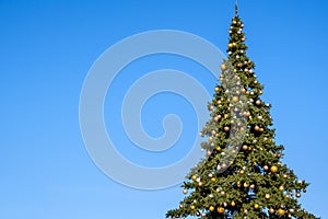 Many New Year decorations and garland on a big artificial Christmas tree outdoors on a blue sky background. At sunny summer day