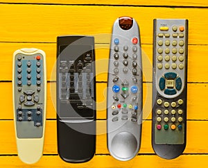 Many obsolete TV remotes on a yellow rustic wooden table. Top view.