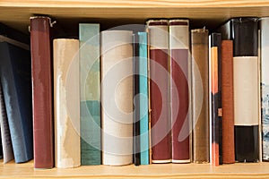 Many old dusty books in a library on a wooden shelve