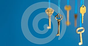 Many old keys of yellow gold color are hanging on thread on a blue background. The concept of the selection of access or password