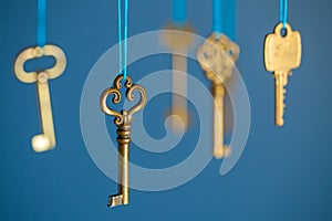 Many old keys of yellow gold color are hanging on thread on a blue background. The concept of the selection of access or password