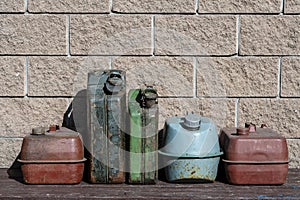 Many old rusty iron fuel cans on a table near the garage, closeup. Various metal painted canisters for gasoline, retro style