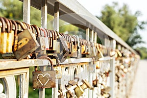 Many old rusty metal locks closed on fence of bridge over river. Love forever through time concept