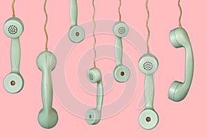 Many old telephone handsets from rotary landlines hanging from cords on pink background. Plastic grey removed receiver