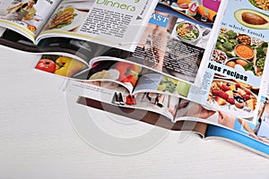 Many open magazines on white wooden table, above view
