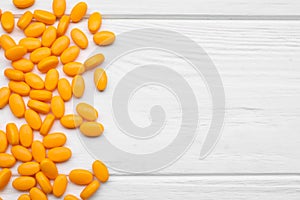 Many orange dragee candies on white wooden table, flat lay. Space for text
