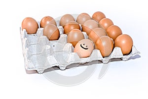 Many orange spotted brown chicken eggs in carton open box container on white background. One egg with drawn smile