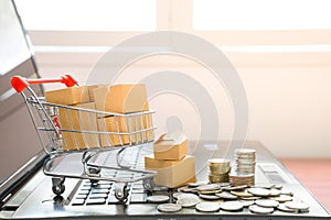 Many parcel boxes in a shopping cart and coins stack on laptop computer  for online shopping concept